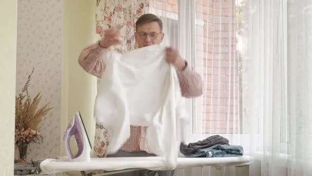 Een man lijnen zijn shirt op de strijkplank in zijn huis — Stockvideo