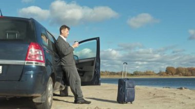 İş adamı arabasının yakınında sahilde rahatlatıcı çalışma bir laptop çanta.