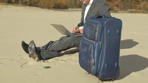 Empresario con una maleta portátil trabajando relajado en la playa — Vídeos de Stock