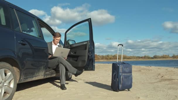 彼の車の近くのビーチでリラックスの作業ノート パソコン スーツケースを持ったビジネスマン. — ストック動画