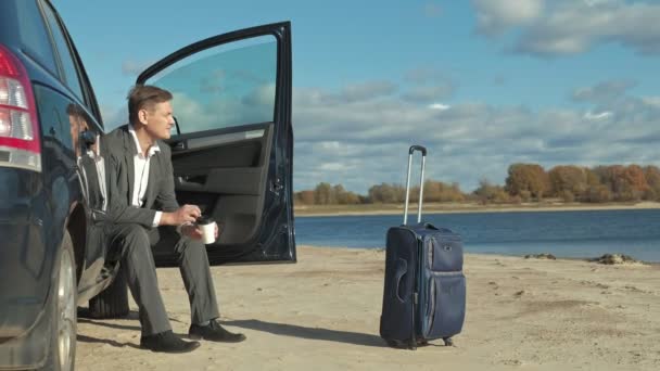 Empresário com uma mala de laptop trabalhando relaxante na praia perto de seu carro . — Vídeo de Stock