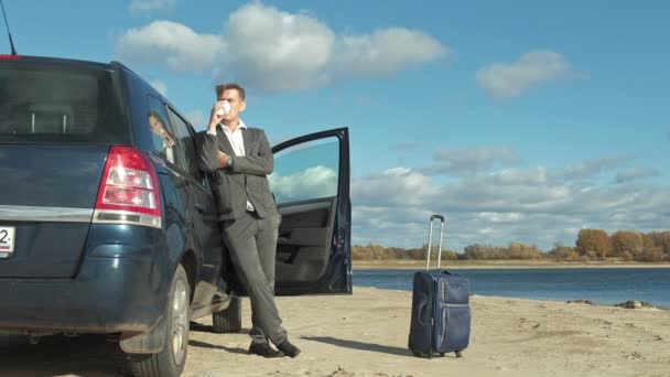 Empresario con una maleta portátil trabajando relajado en la playa cerca de su coche . — Vídeo de stock