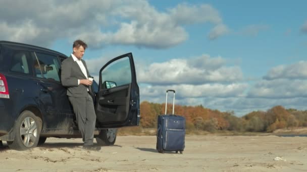 Επιχειρηματίας με μια βαλίτσα lap-top εργασίας χαλάρωση στην παραλία κοντά στο αυτοκίνητό του. — Αρχείο Βίντεο