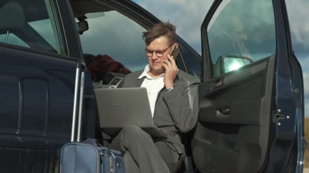 Uomo d'affari con una valigia portatile che lavora rilassandosi sulla spiaggia vicino alla sua auto . — Video Stock