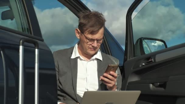 Geschäftsmann mit Laptop-Koffer entspannt am Strand in der Nähe seines Autos. — Stockvideo