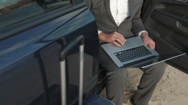 İş adamı arabasının yakınında sahilde rahatlatıcı çalışma bir laptop çanta.