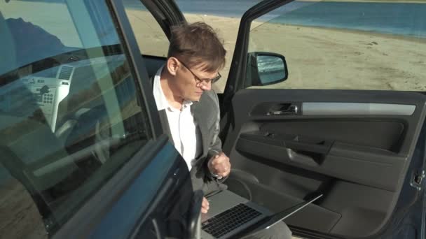 Uomo d'affari con una valigia portatile che lavora rilassandosi sulla spiaggia vicino alla sua auto . — Video Stock