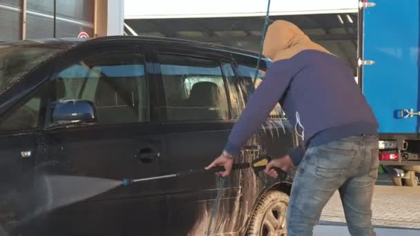 Мужчина моет свою машину под водой высокого давления на открытом воздухе — стоковое видео