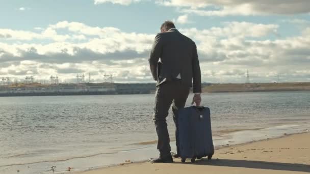 Empresario con una maleta portátil trabajando relajado en la playa — Vídeo de stock