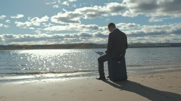 Uomo d'affari con una valigia portatile che lavora rilassandosi sulla spiaggia — Video Stock