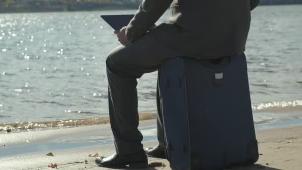 Empresario con una maleta portátil trabajando relajado en la playa — Vídeos de Stock