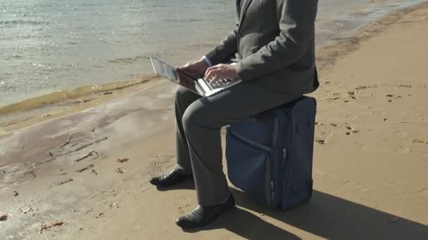 Бізнесмен з валізою для ноутбуків, що працює розслабляючись на пляжі — стокове відео