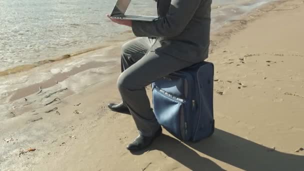 Empresario con una maleta portátil trabajando relajado en la playa — Vídeo de stock