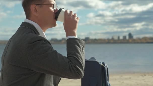 Empresario con una maleta portátil trabajando relajado en la playa — Vídeos de Stock