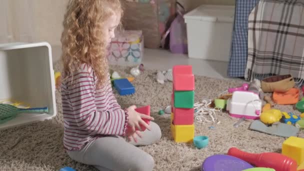 Beau petit enfant riant, blond préscolaire, jouant avec des jouets colorés, assis sur le sol dans la chambre — Video
