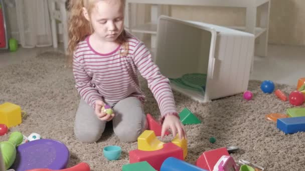 Precioso niño riendo, rubia preescolar, jugando con juguetes coloridos, sentado en el suelo en la habitación — Vídeos de Stock