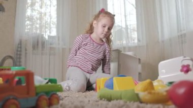 Güzel gülüyor küçük çocuk, okul öncesi sarışın renkli oyuncaklar, 4 k odasında katta oturan oynarken,