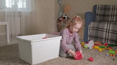 Güzel gülüyor küçük çocuk, okul öncesi sarışın, oda katta oturan beyaz kutu içinde renkli oyuncaklar ile oynama