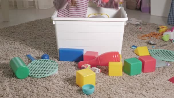 Härlig skrattar lite kid, förskola blond, leker med färgglada leksaker i en vit ruta, sitter på golvet i rummet — Stockvideo