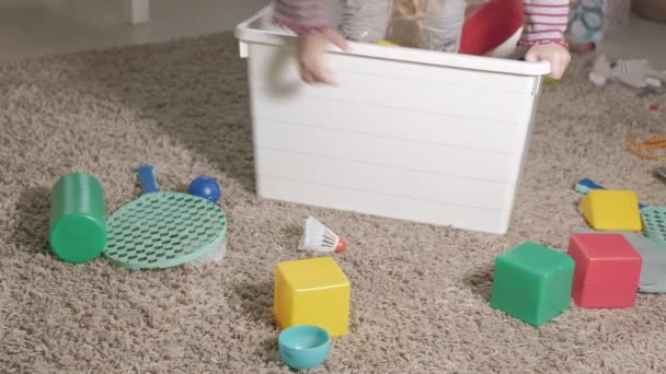 Beau petit enfant riant, blonde préscolaire, jouant avec des jouets colorés dans une boîte blanche, assis sur le sol dans la chambre — Video