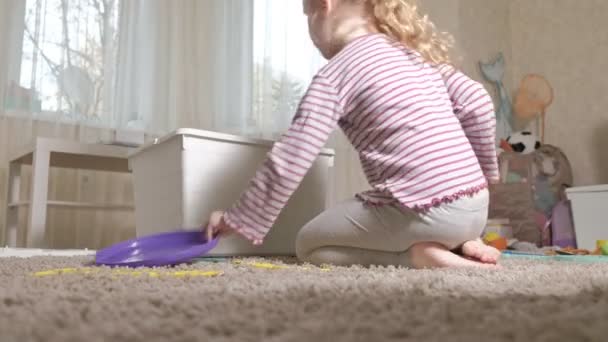 Bella ridendo bambino piccolo, prescolare bionda, giocando con i giocattoli colorati in una scatola bianca, seduto sul pavimento nella stanza — Video Stock