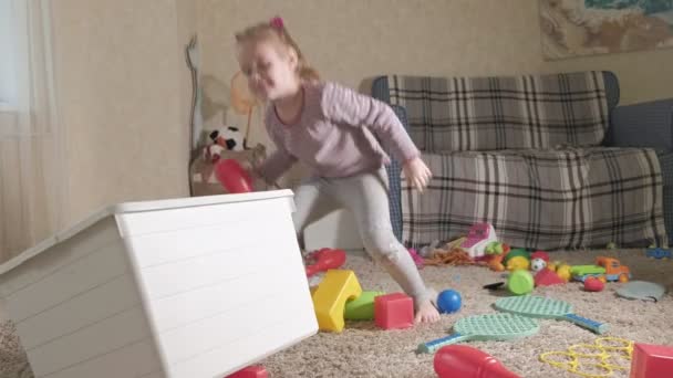 Linda criança rindo, loira pré-escolar, brincando com brinquedos coloridos em uma caixa branca, sentada no chão na sala — Vídeo de Stock