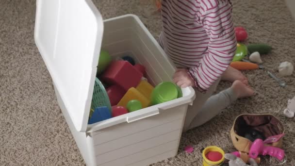 Linda criança rindo, loira pré-escolar, brincando com brinquedos coloridos, sentada no chão na sala — Vídeo de Stock