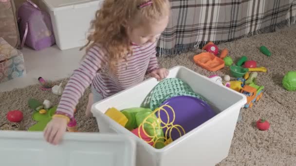 Милый смеющийся малыш, блондинка в детском саду, играющая с красочными игрушками, сидящая на полу в комнате — стоковое видео
