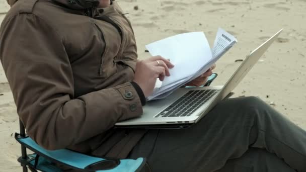 Mature businessman sitting and relaxing near a river. Man in a warm jacket and using laptop. — Stock Video