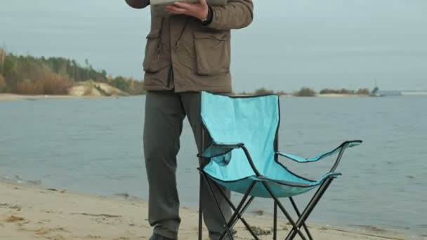 Ältere Geschäftsleute sitzen und entspannen in der Nähe eines Flusses. Mann in warmer Jacke und mit Laptop. — Stockvideo