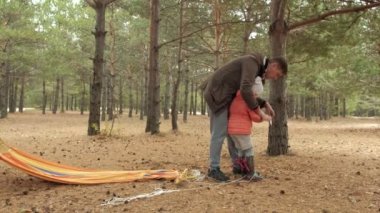 Genç bir adam ormanda hamak ayarlar. Yakın kızı yürür.