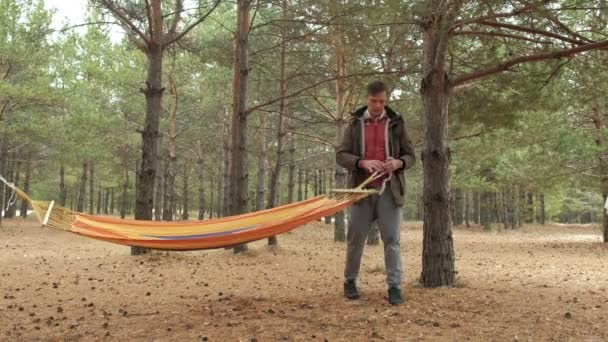 En ung man i skogen ställer en hängmatta — Stockvideo