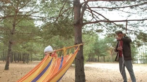 Un giovane uomo nel bosco mette amaca. Figlia passeggiate nelle vicinanze . — Video Stock