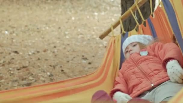 Чарівна дитина сидить в гамаку під деревами — стокове відео