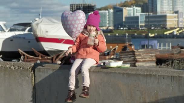 Маленькая девочка в розовой шляпе с воздушным шаром в речном порту, обедает , — стоковое видео