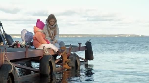 Женщина с девушкой, мать с дочерью, сидеть на мосту, река, пикник, в теплой одежде — стоковое видео