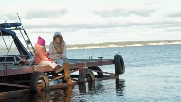 Žena s ženou, matka s dcerou, sedět na most, řeka, piknik, v teplé oblečení — Stock video