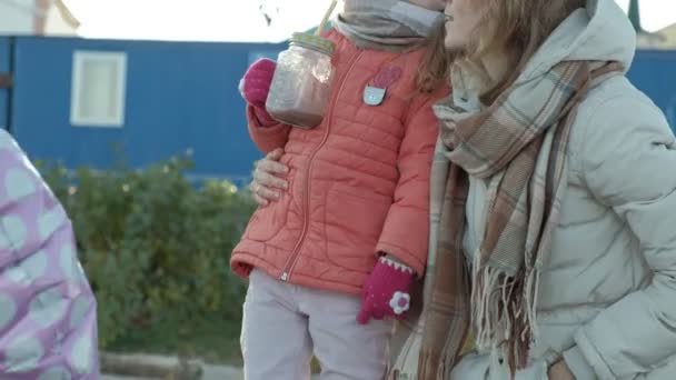 Женщина с девочкой, мать с дочерью, сидящая на речном порту, девушка, пьющая горячую коку, обнимающаяся, улыбающаяся, счастливая, в теплой одежде — стоковое видео