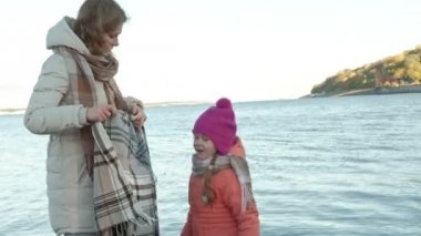 bir kız, bir anne bir kızı olan bir kadınla bekliyoruz nehir noktasındaki elele, sarılma, gülümseyen, mutlu, sıcak giysiler, kendileri ile Halı kaplama