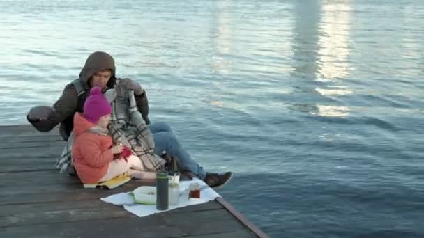 Muž a dívka, otec a dcera, sedět v říční přístav, pít čaj, piknik, smát se, v teplé oblečení — Stock video