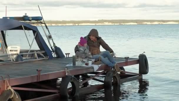 Człowiek i dziewczyna, ojciec i Córka, siedzieć w port rzeczny, pić herbatę, piknik, śmiech, w ciepłe ubrania — Wideo stockowe