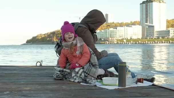 Erkek ve kız, baba ve kızı nehir limanı içinde oturup, çay içmek, piknik, gülmek, sıcak giysiler içinde — Stok video
