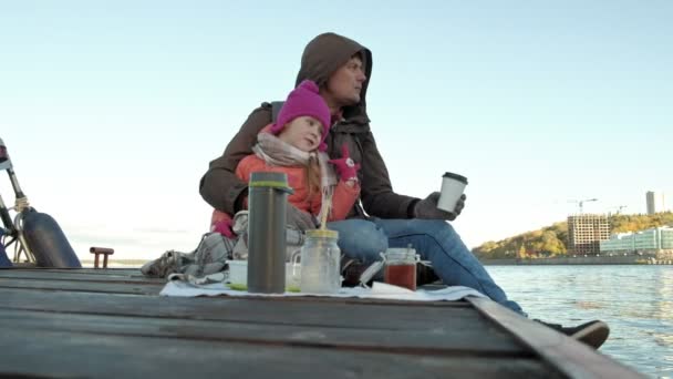 Uomo e ragazza, padre e figlia, sedersi nel porto del fiume, bere il tè, pic-nic, ridere, in abiti caldi — Video Stock