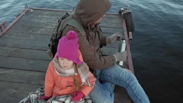 Hombre y chica, padre e hija, sentarse en el puerto del río, beber té, picnic, reír, en ropa de abrigo — Vídeos de Stock