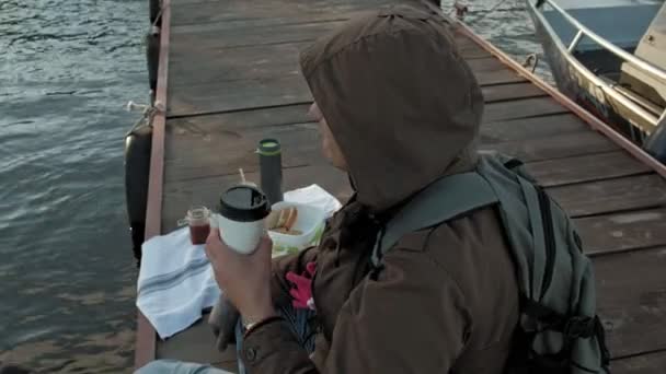 Man and girl, father and daughter, sit in the river port, drink tea, picnic, laugh, in warm clothes — Stock Video