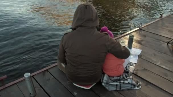 Homem e menina, pai e filha, sentar-se no porto do rio, beber chá, piquenique, rir, em roupas quentes — Vídeo de Stock