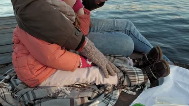 Hombre y chica, padre e hija, sentarse en el puerto del río, beber té, picnic, reír, en ropa de abrigo — Vídeos de Stock