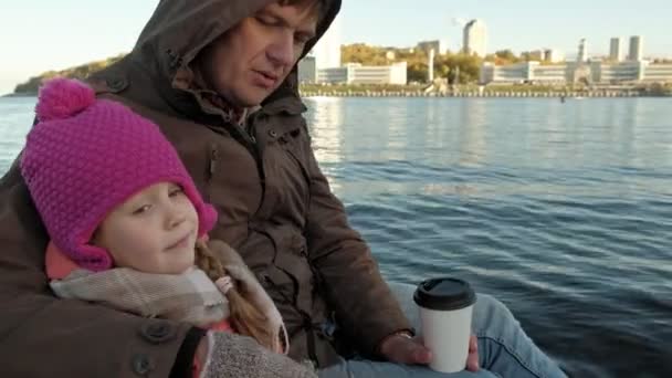 Erkek ve kız, baba ve kızı nehir limanı içinde oturup, çay içmek, piknik, gülmek, sıcak giysiler içinde — Stok video