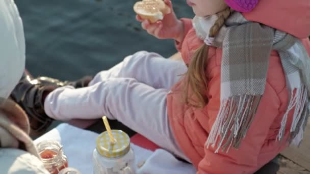 Kvinna med flicka, mor med dotter sitta på bron, floden, picknick, i varma kläder — Stockvideo