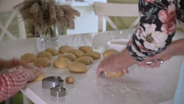 Liten flicka och hennes mormor göra kakor från degen när du står i köket — Stockvideo